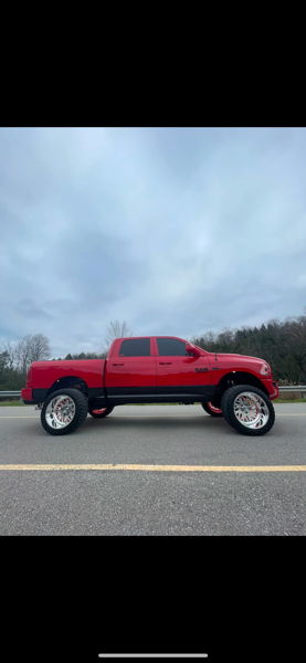 Side profile of lifted red RAM 1500 with chrome wheels and off-road tires on rural road