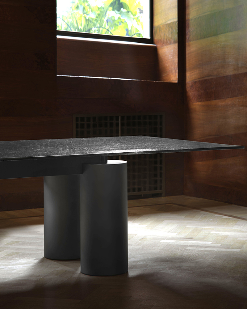 Modern Serenissimo table with a dark surface and cylindrical base in a wooden room.