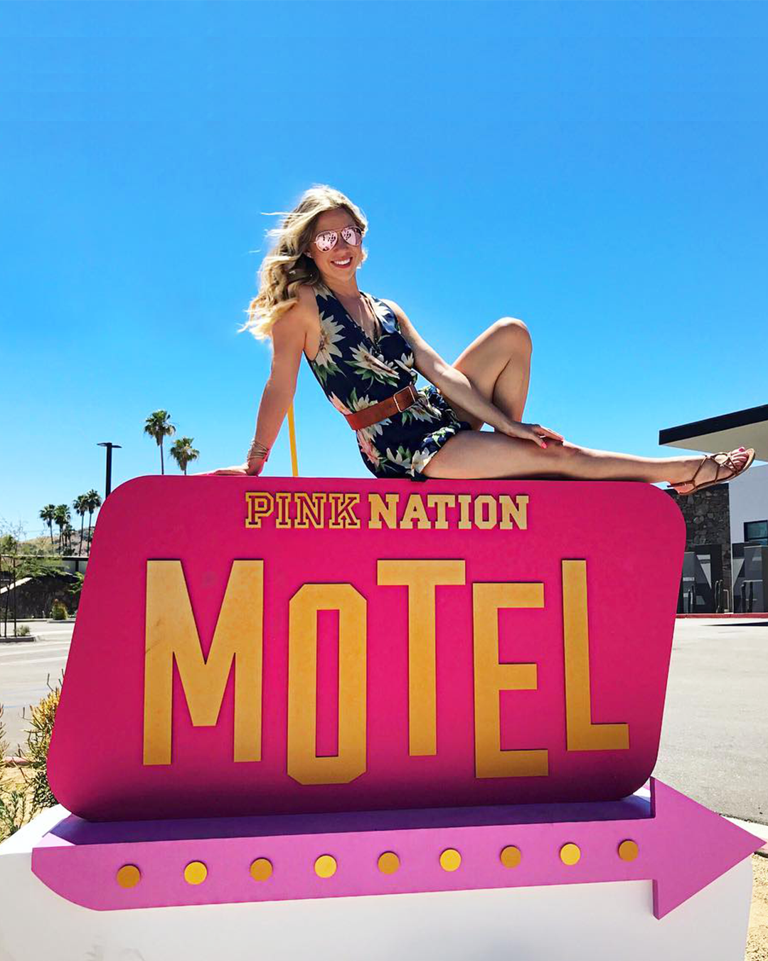 Image of a Blonde haired model sitting on top of got pink sign that reads 