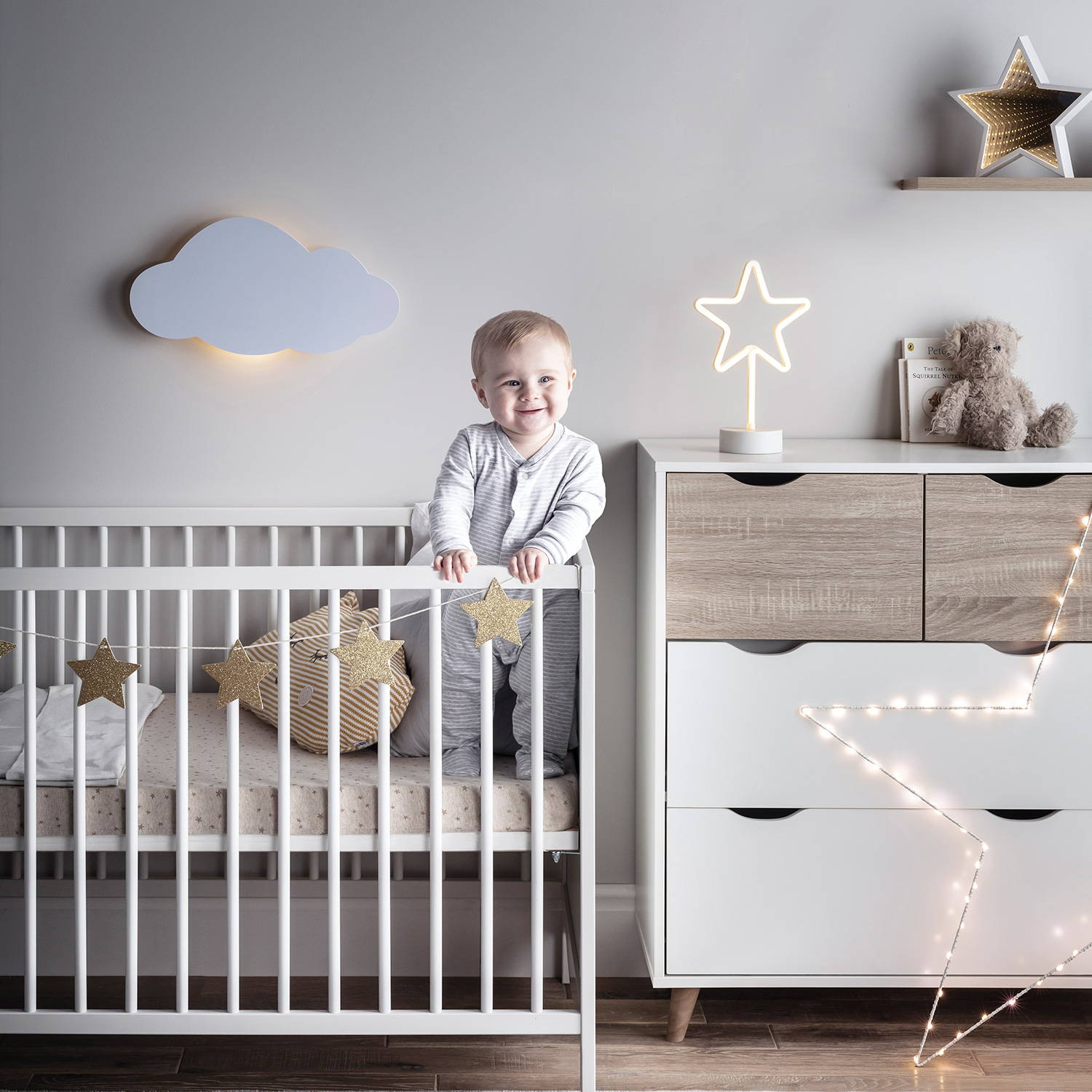 Kleinkind im Kinderbett, umgeben von einer Wolken-Wandlampe und verschiedenen Sternenlichtern