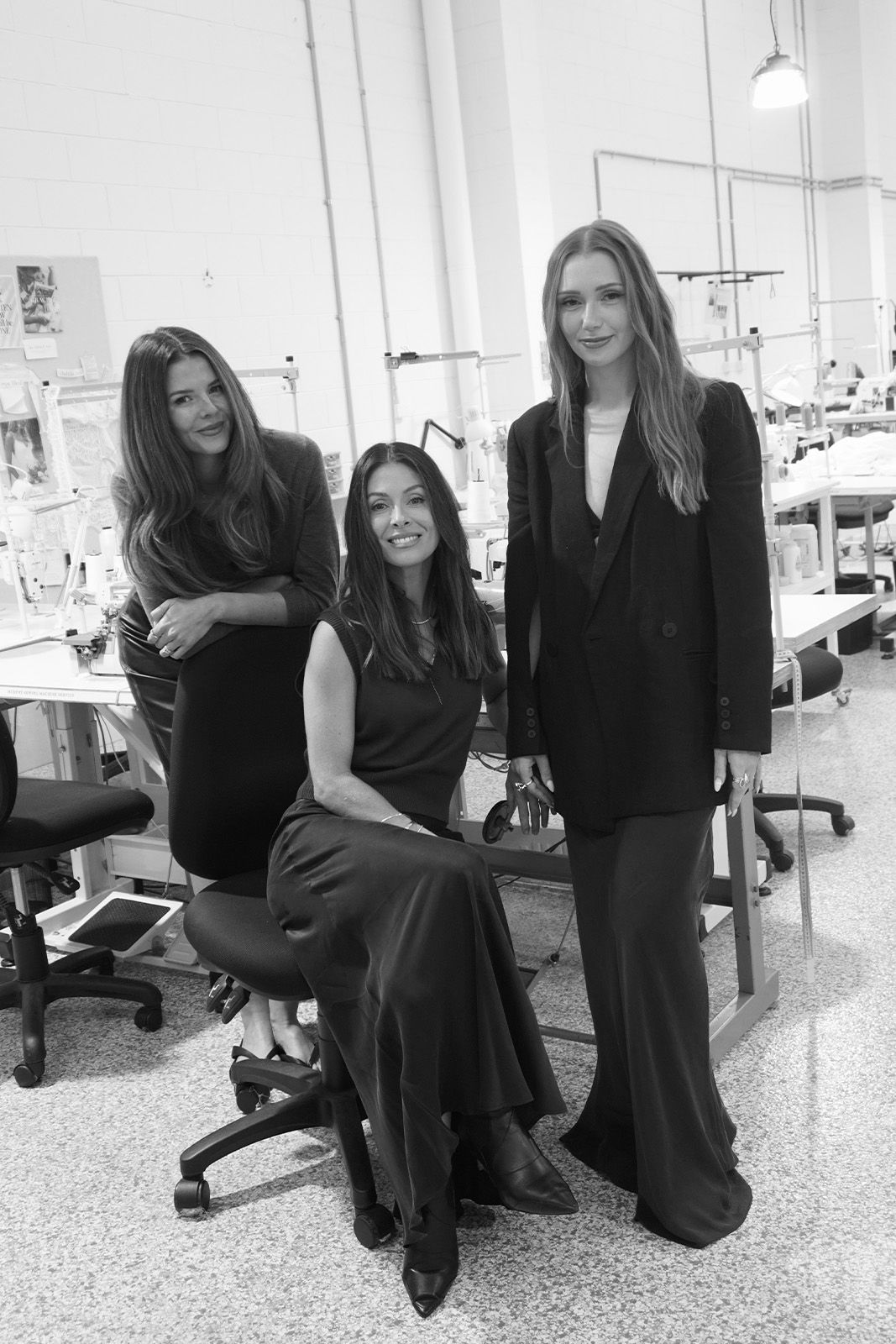 Three women in elegant black dresses posing in a studio setting.