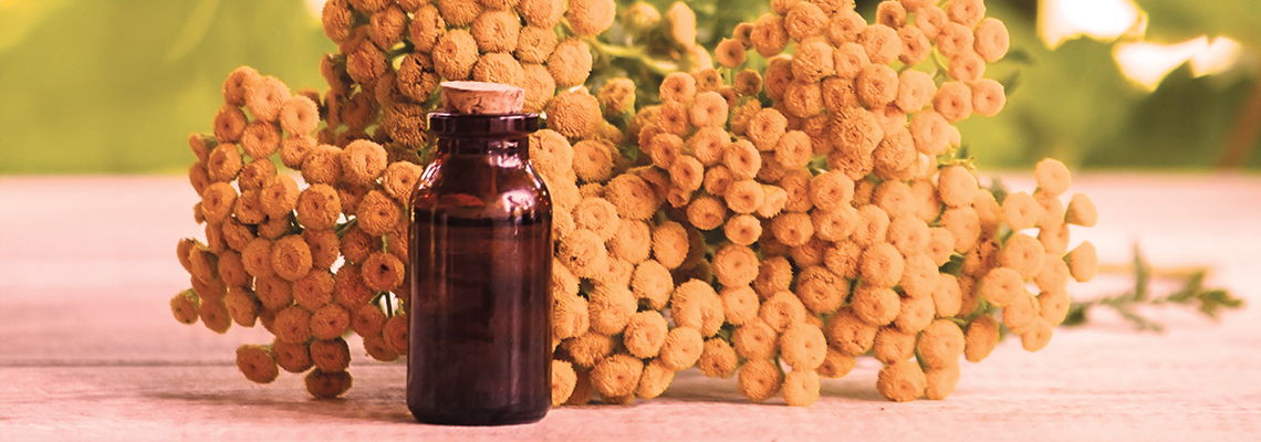 Brown bottle in front of yellow flowers on a light surface.