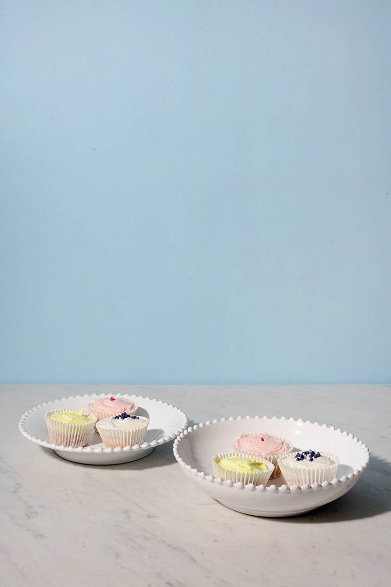 A pearl white soup plate and a pasta plate, both filled with cupcakes.