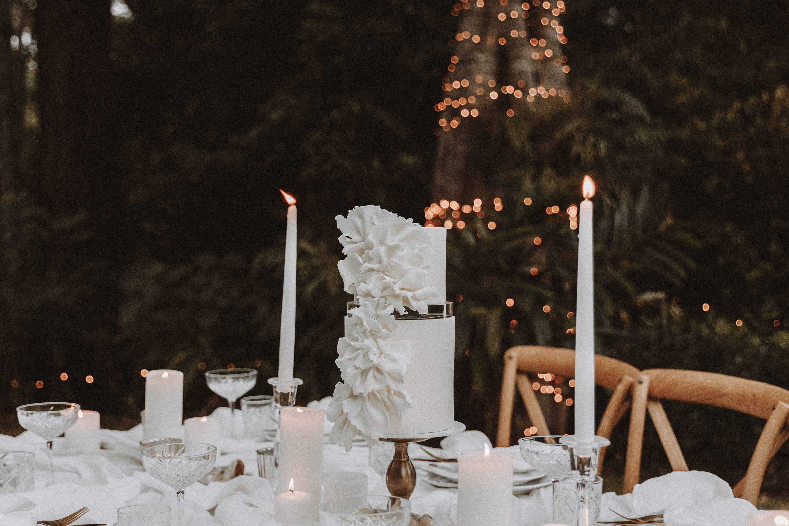 White wedding cake with white florals and candles on wedding table.
