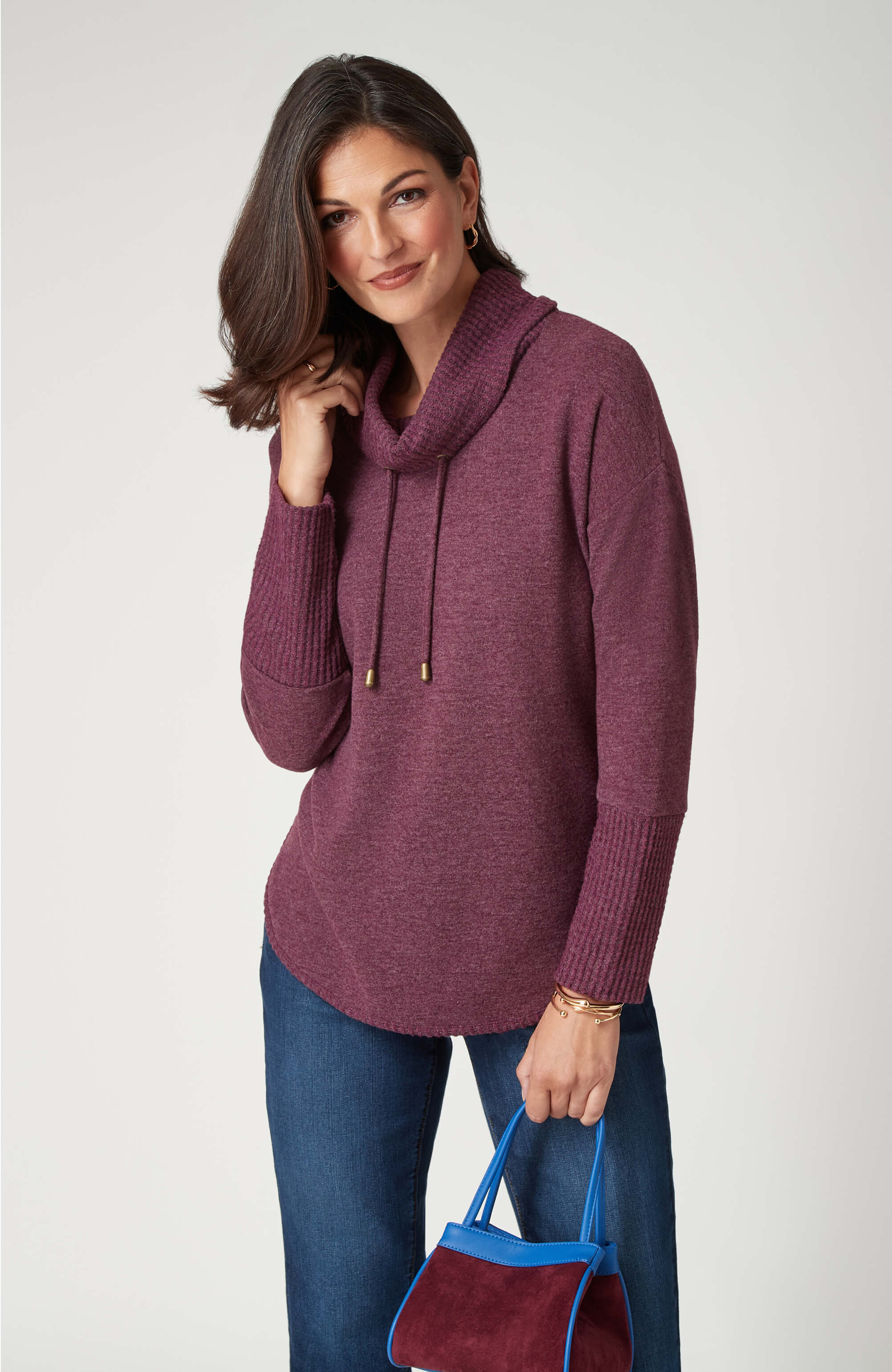 Woman in a maroon sweater with a blue handbag, smiling at the camera.