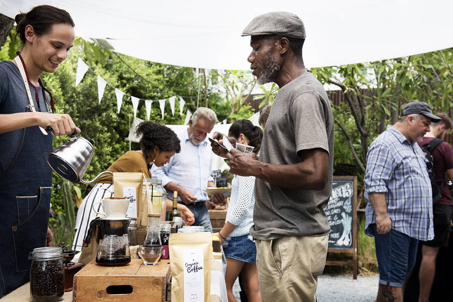 man smiling and pouring coffee at a local market for customer
