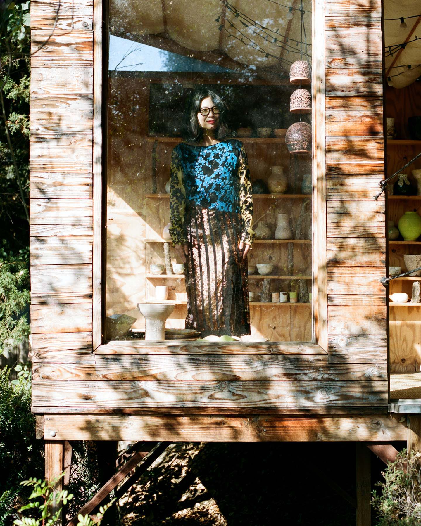 An image of Raina Lee standing in her treehouse wearing a sequined dress by Rachel Comey.