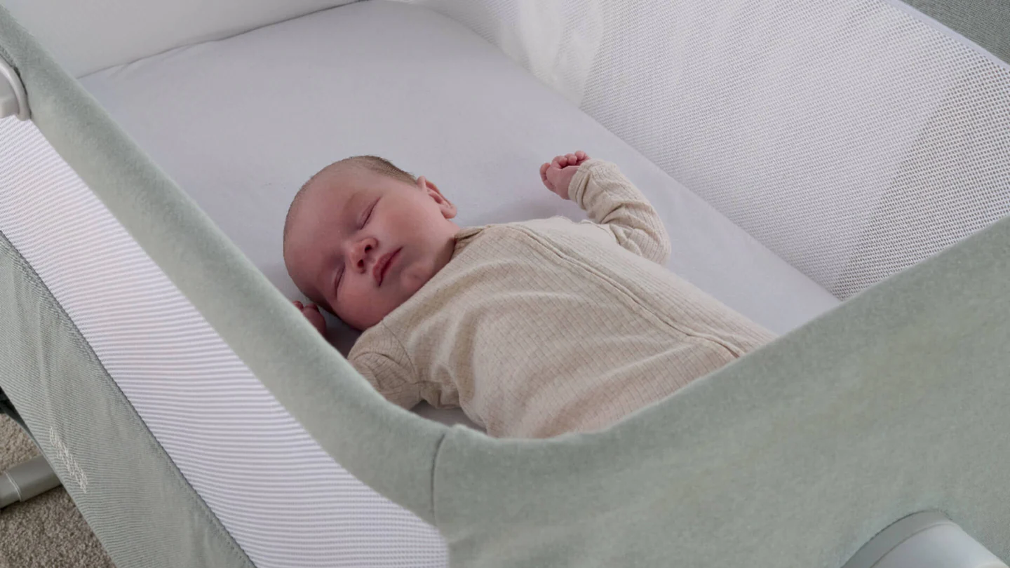 A sleeping baby in a light-colored bassinet.