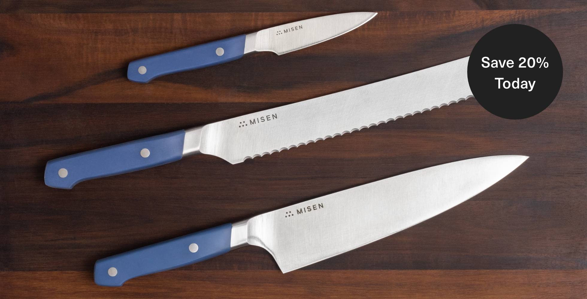 Misen Chef’s, Serrated, and Paring Knives seen from above on a dark wood cutting board, with a badge calling out 20% savings.