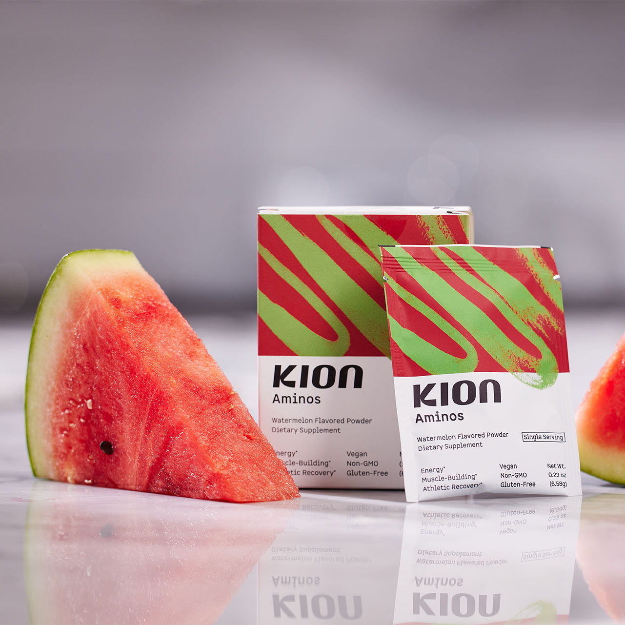 Two KION product boxes beside a slice of watermelon on a reflective surface.
