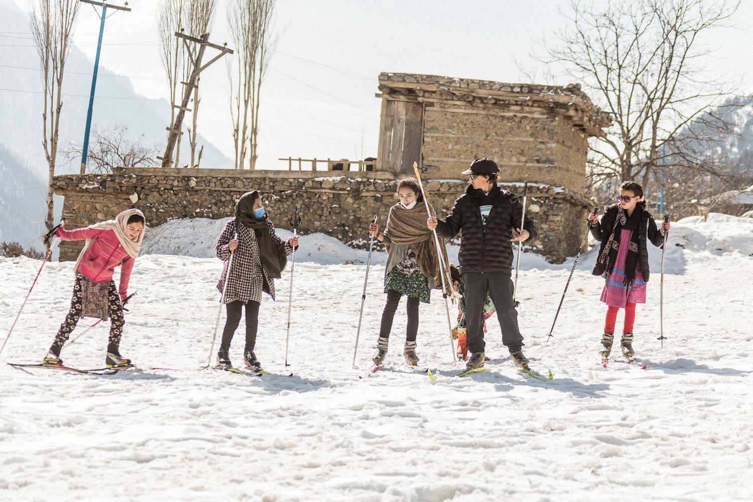 Group of people skiing on snow with a cabin in the background.