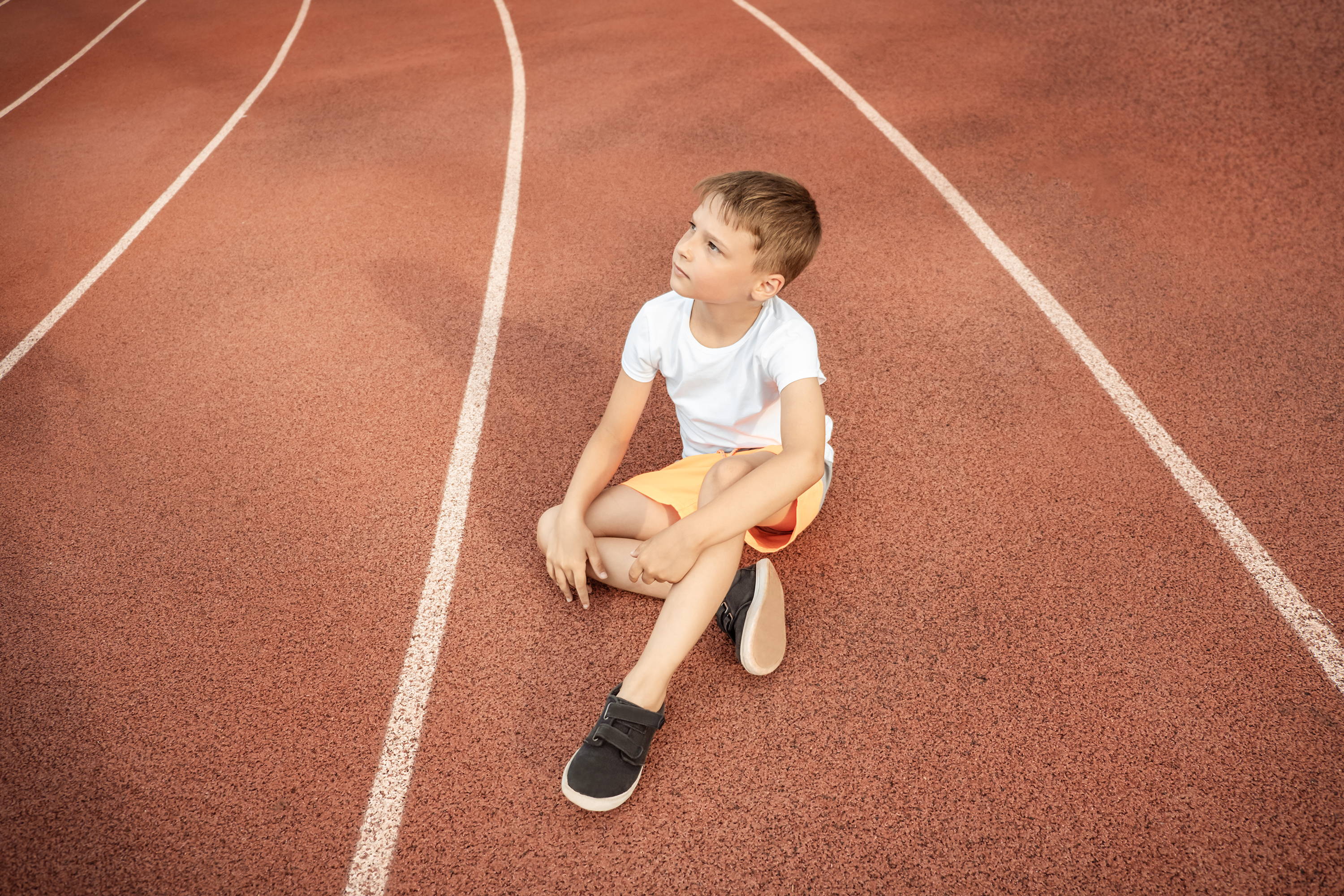 Jongetje dat midden op een atletiekbaan zit – lichamelijke beweging kan astma uitlokken; misschien moest hij stoppen of kan hij niet meedoen
