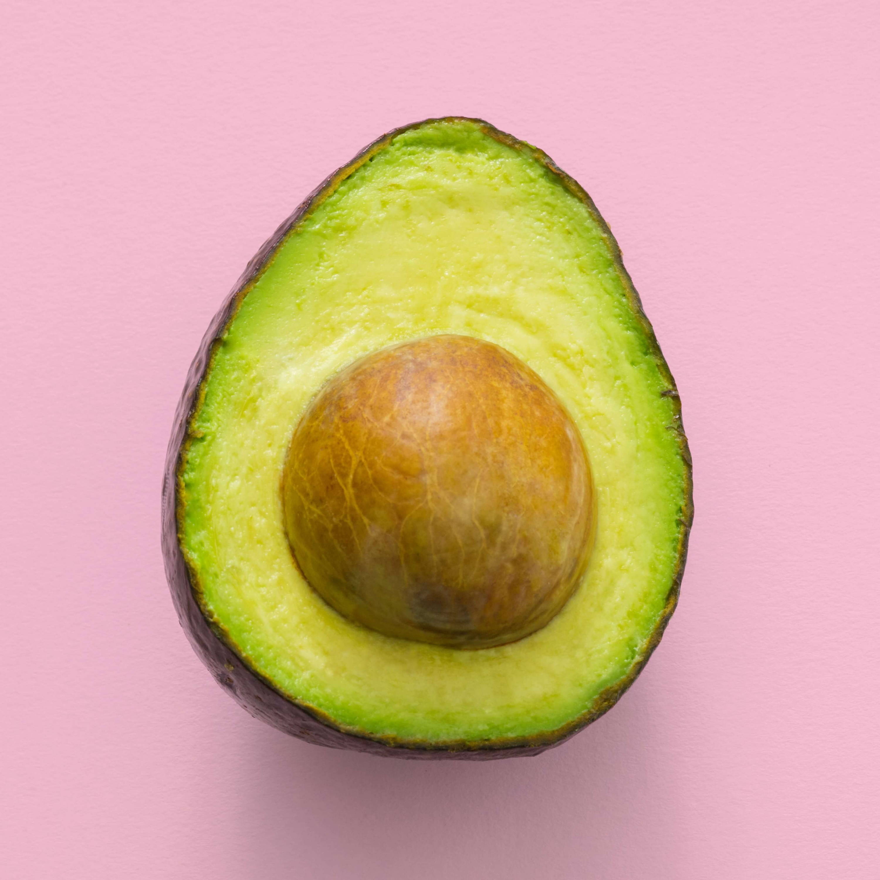A halved avocado on a light pink background. 