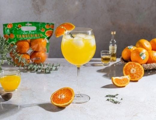 A glass of orange drink with fresh oranges and a bag of mandarins.