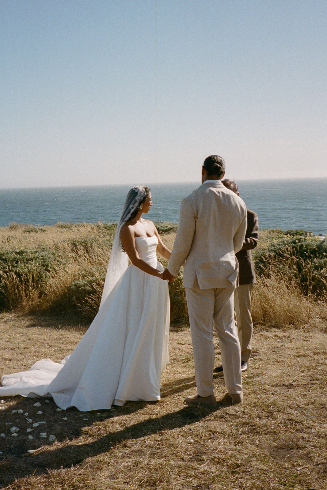 A couple holding hands during a wedding ceremony by the ocean.