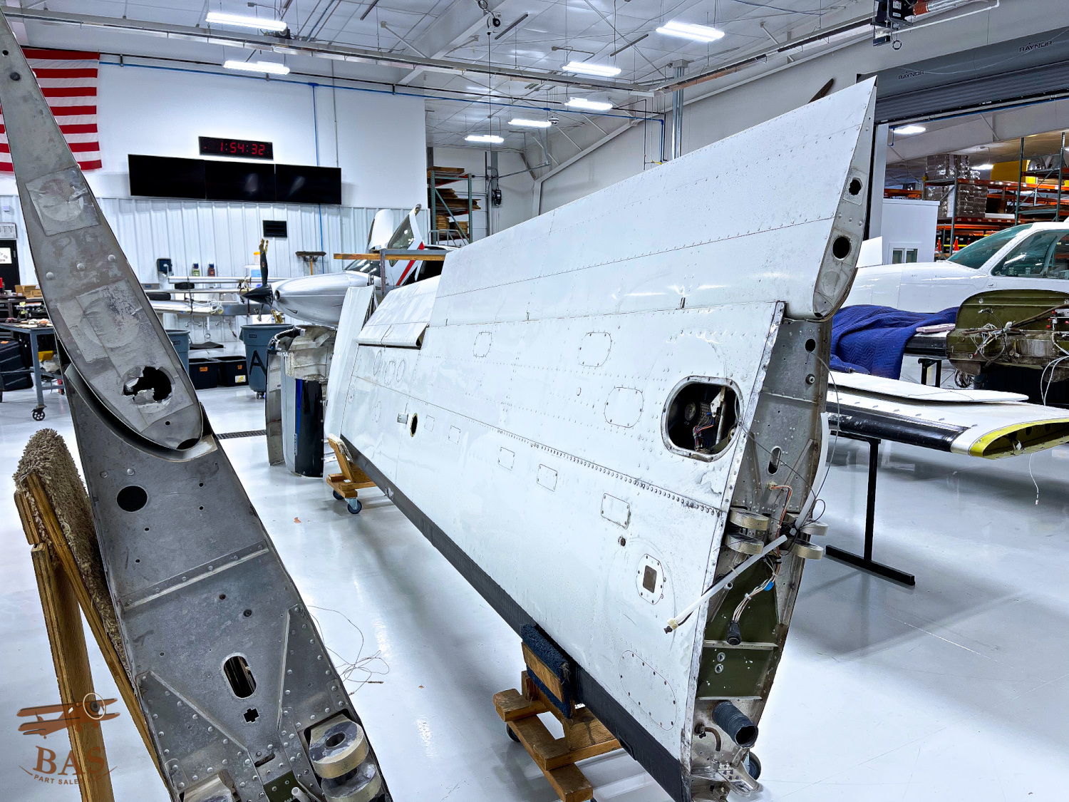 Aircraft wing section displayed in a hangar with various tools and vehicles.