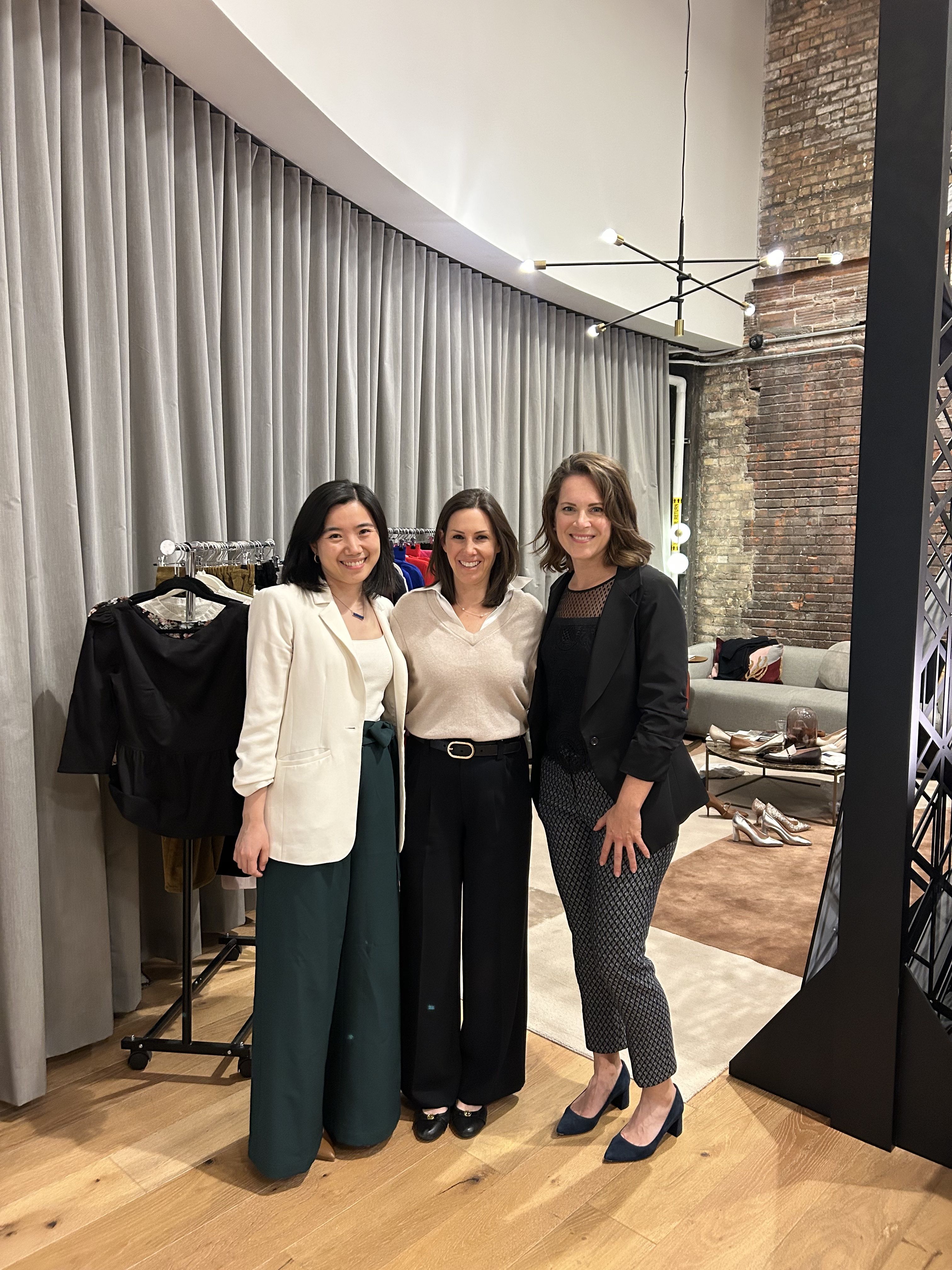 Three women posing together in a modern interior setting.