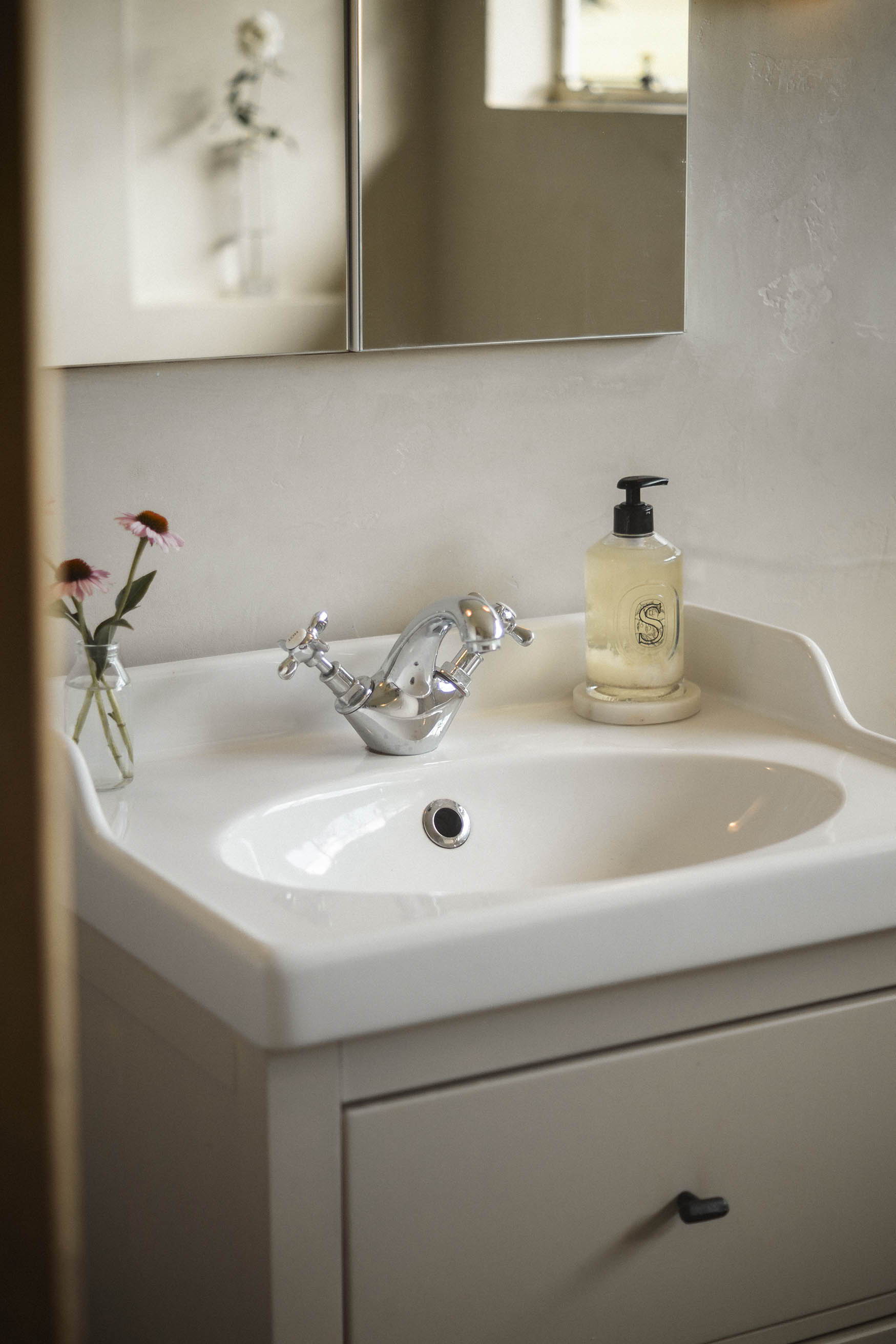 A bathroom sink with a soap dispenser and flowers in a vase.