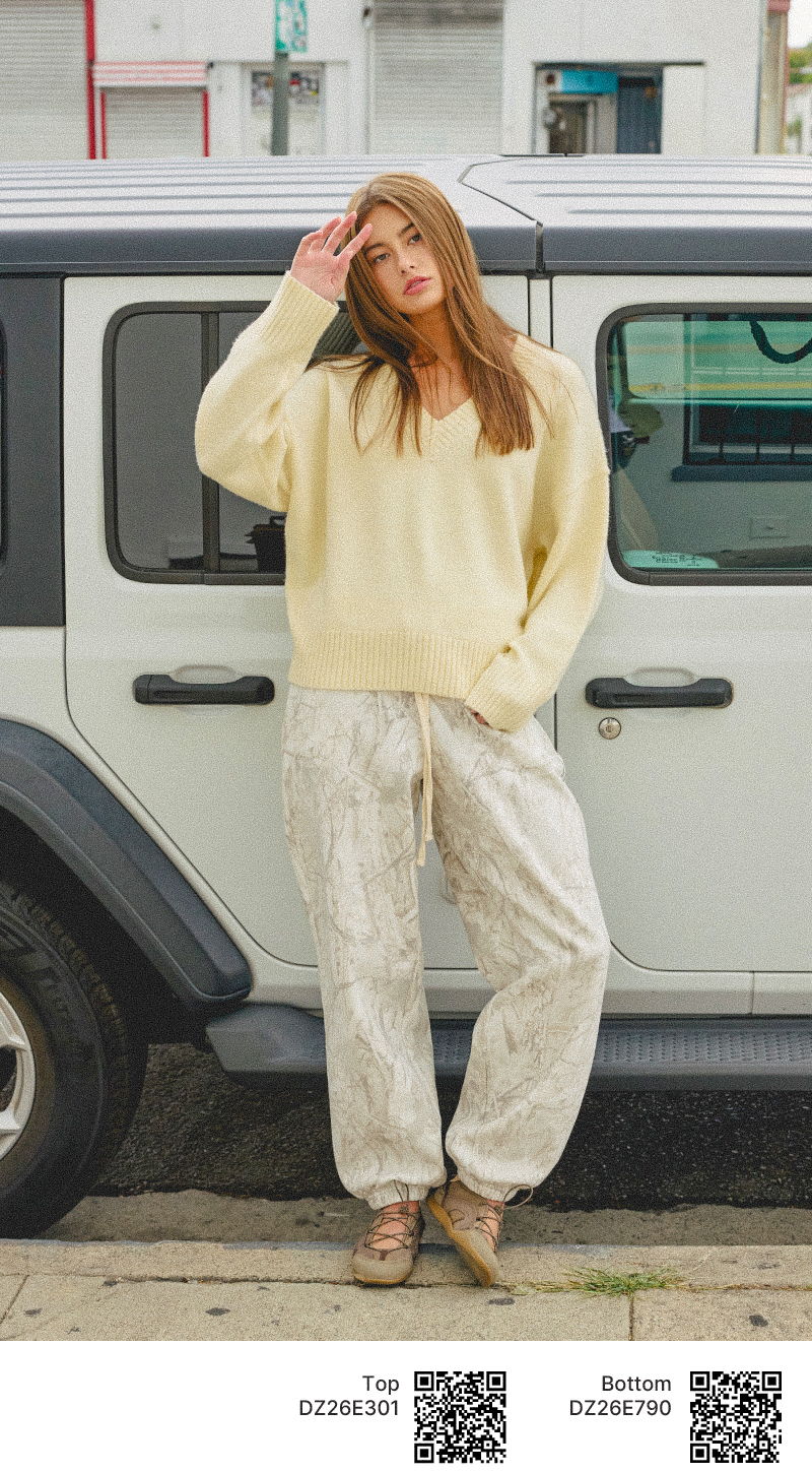 Woman in a yellow sweater and light pants poses beside a vehicle.