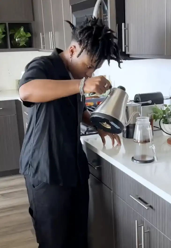 Person pouring coffee from a kettle in a modern kitchen.