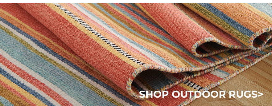A stack of cushions and colorful outdoor rugs for sale.