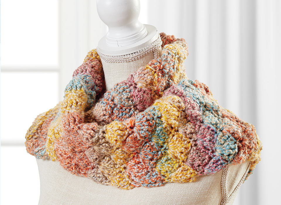 Colorful knitted scarf displayed on a mannequin against a light background.