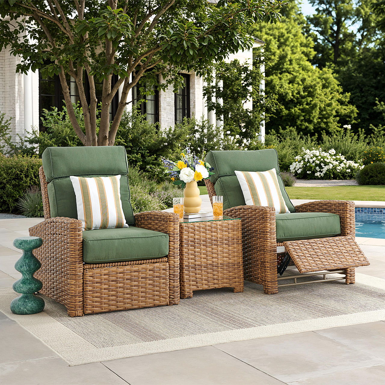 Two wicker chairs with green cushions beside a small table outdoors.