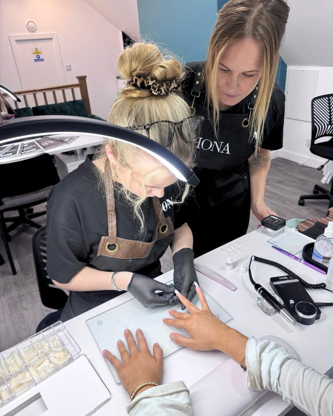 Two nail technicians applying manicure to a client's hand in a salon.