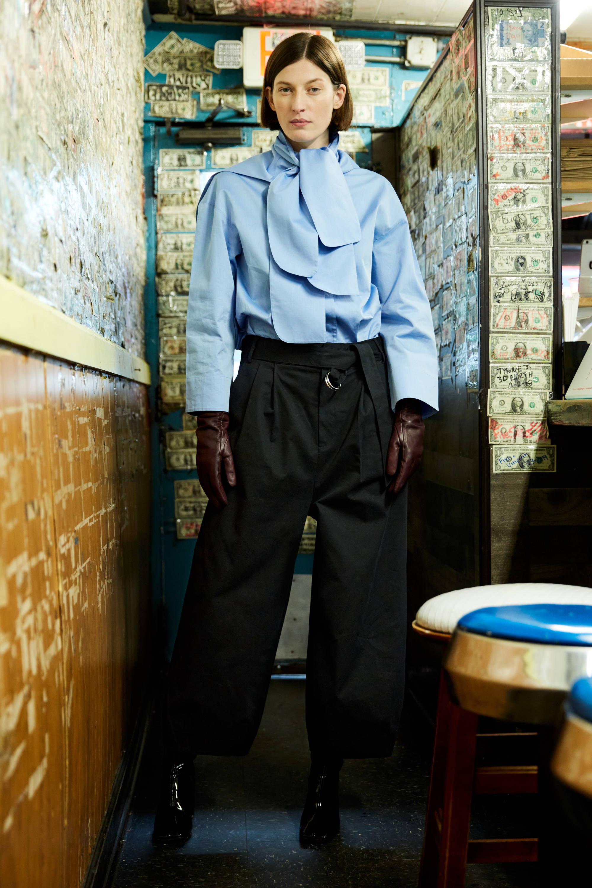 Model wearing a blue blouse and black wide-leg pants in a vintage setting.