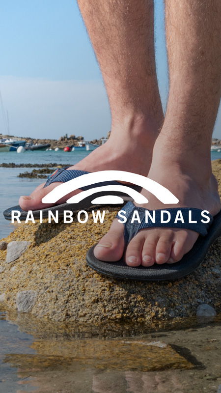 Person wearing flip-flops standing on a rock by the water.