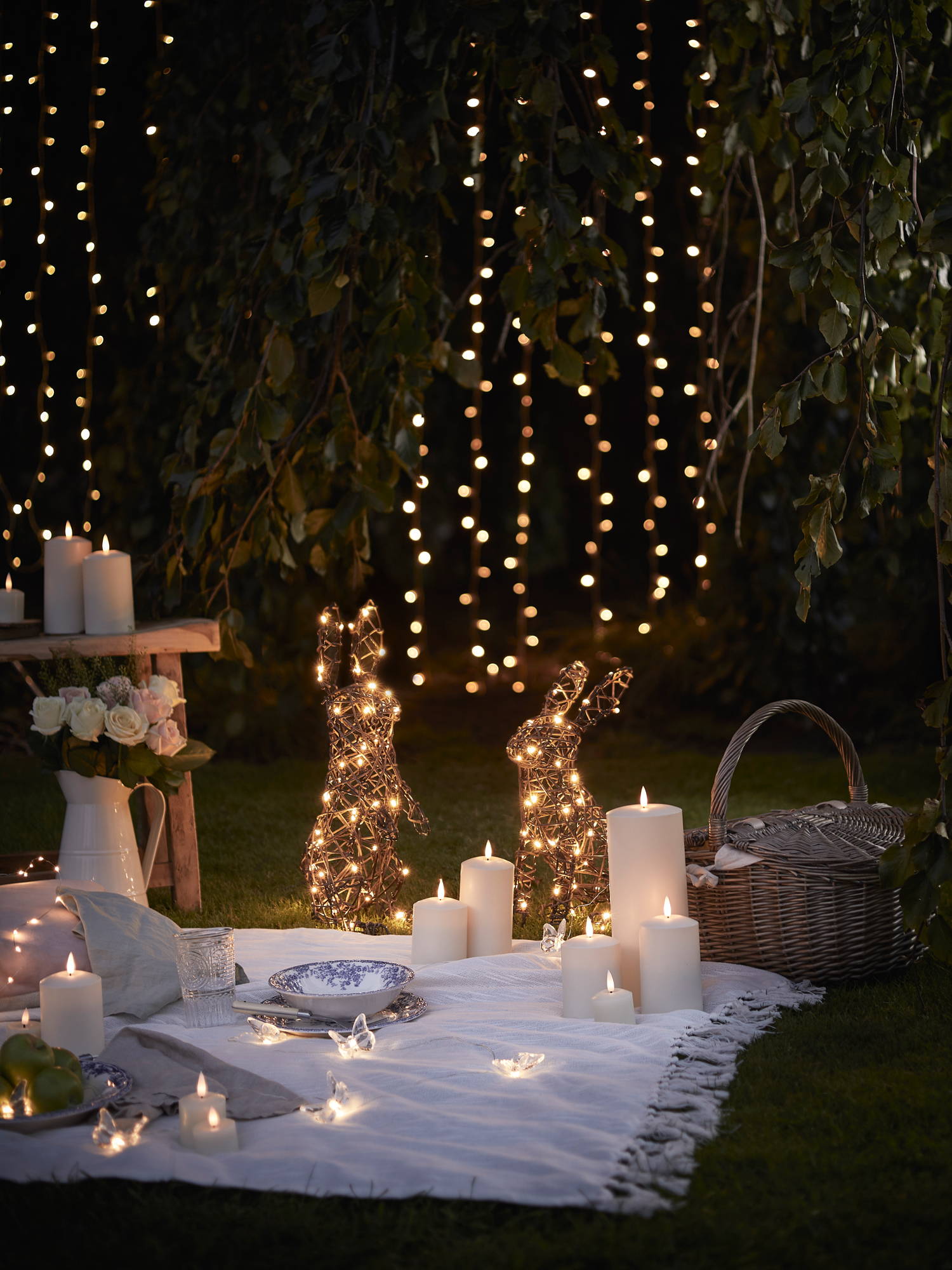 Easter picnic night time setting with rattan bunnies illuminated with TruGlow candles and butterfly micro lights illuminated 