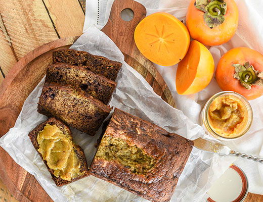 Sliced bread loaf with persimmons and spread on a wooden board.