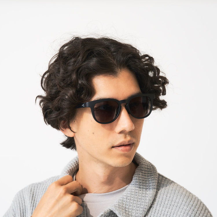 Young man with curly hair wearing sunglasses and a light sweater.