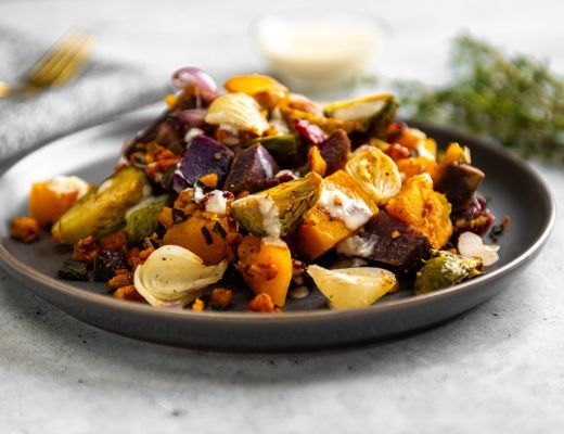 A plate of roasted vegetables with a creamy dressing on the side.