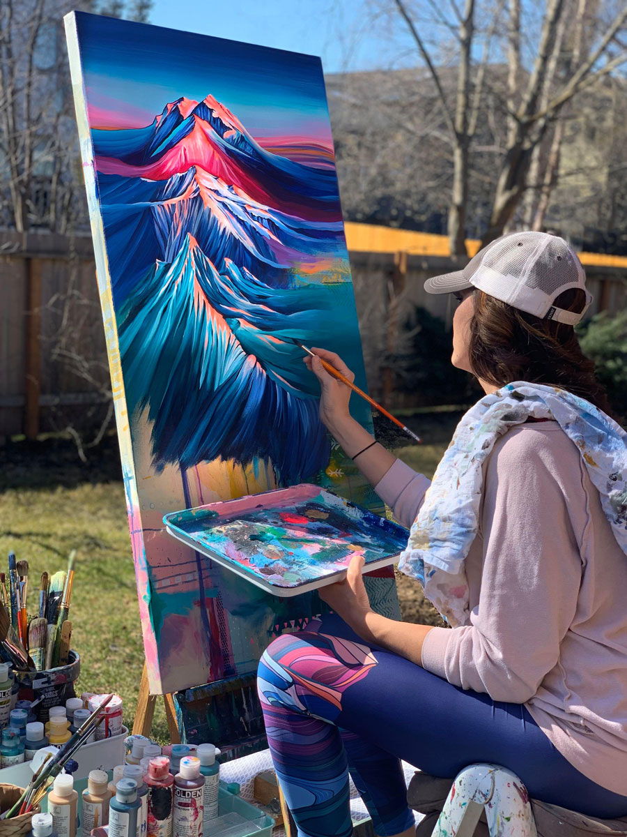 Artist painting a colorful mountain scene outdoors on a sunny day.