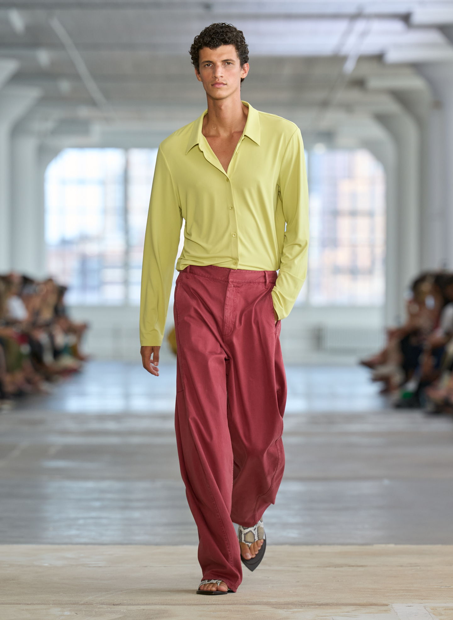 A model walks down the runway wearing a yellow shirt and red pants.