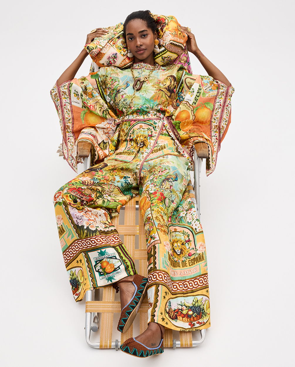 Model in colorful, patterned outfit seated on a chair.