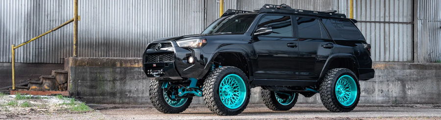 Side view Kealoha's black 2019 Toyota 4Runner lifted turquoise wheels winch bumper roof rack industrial building Conductor's Special 244K Spare Tire Delete featured customer install gallery photo 1