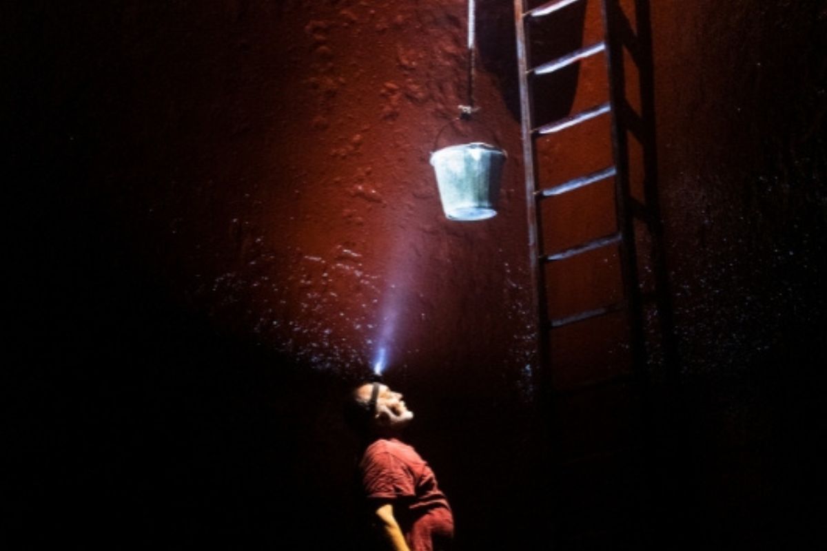 Person looking up at a bucket and ladder in a dark space.