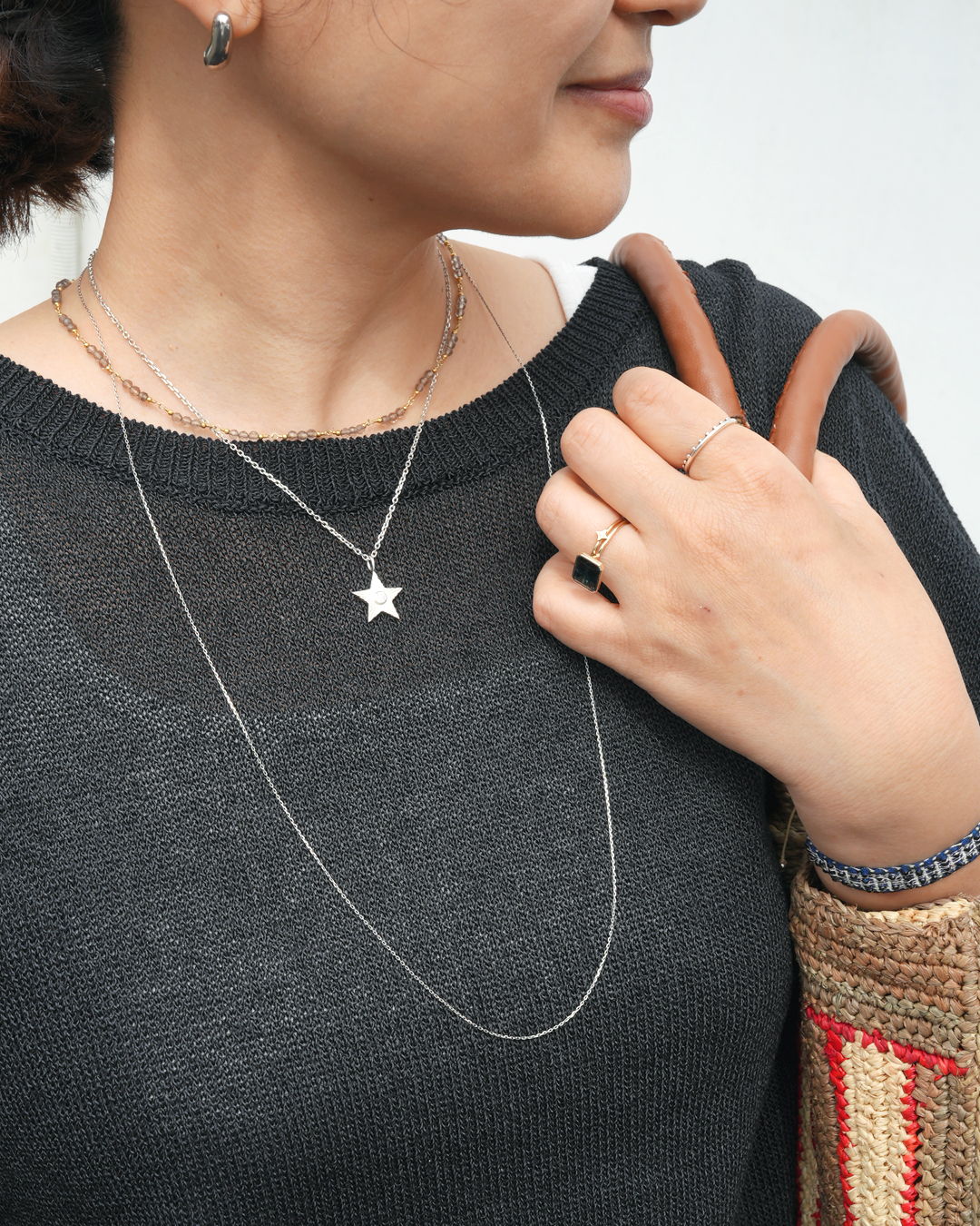 Person wearing a star necklace, holding a bag, in casual attire.