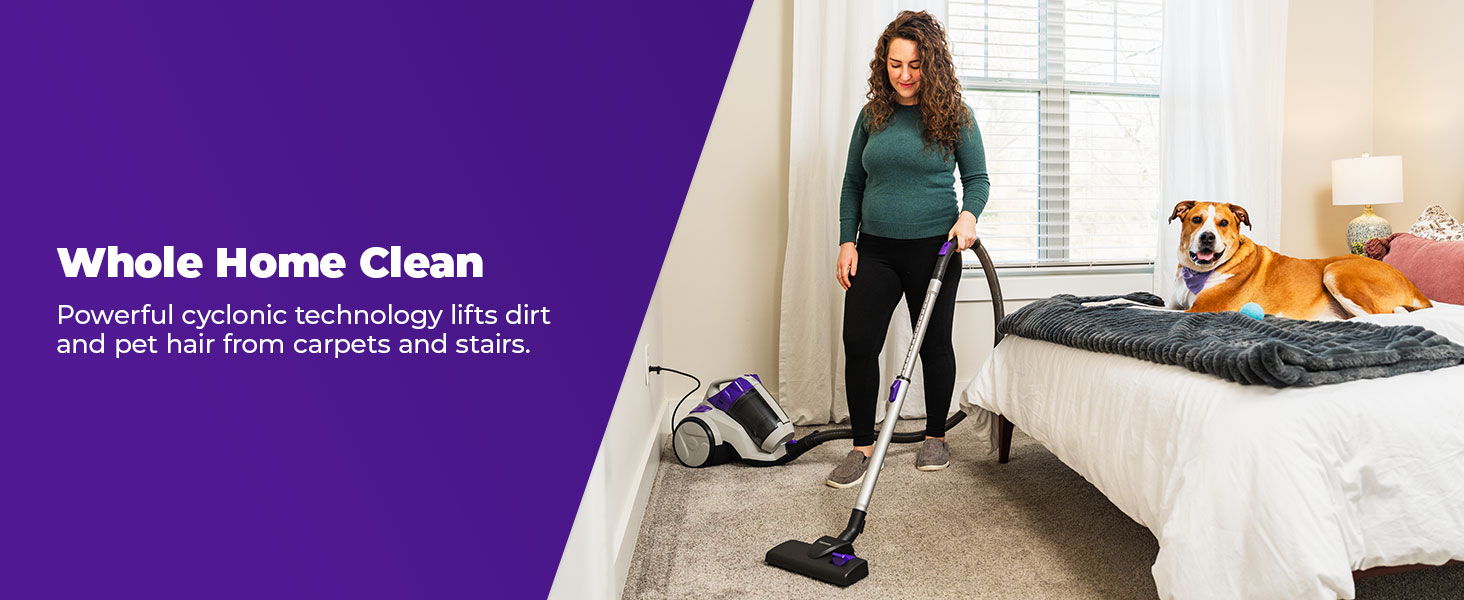 Woman vacuuming a bedroom with a dog on the bed.