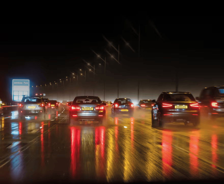 Cars driving on a wet road at night with colorful reflections.