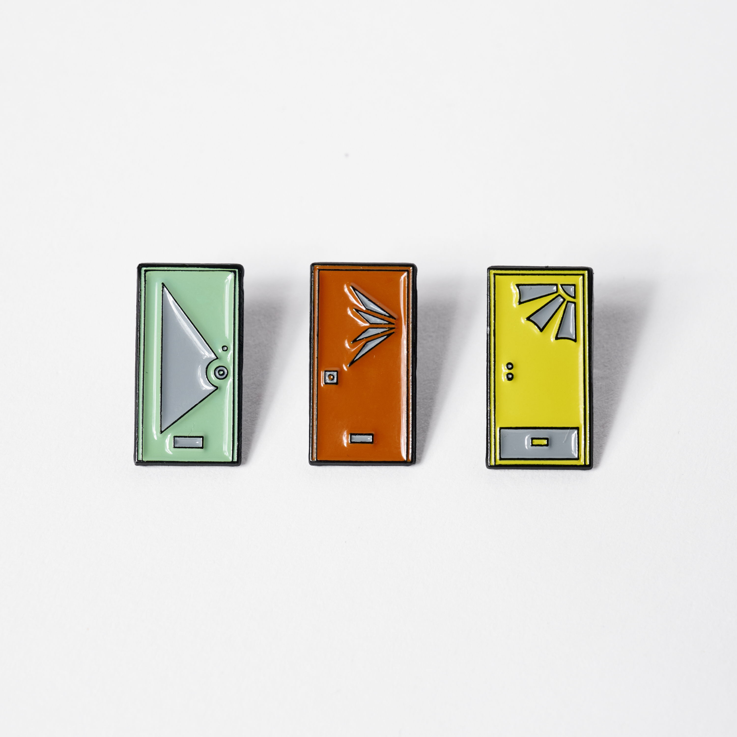Three colorful door-shaped enamel pins with unique designs.
