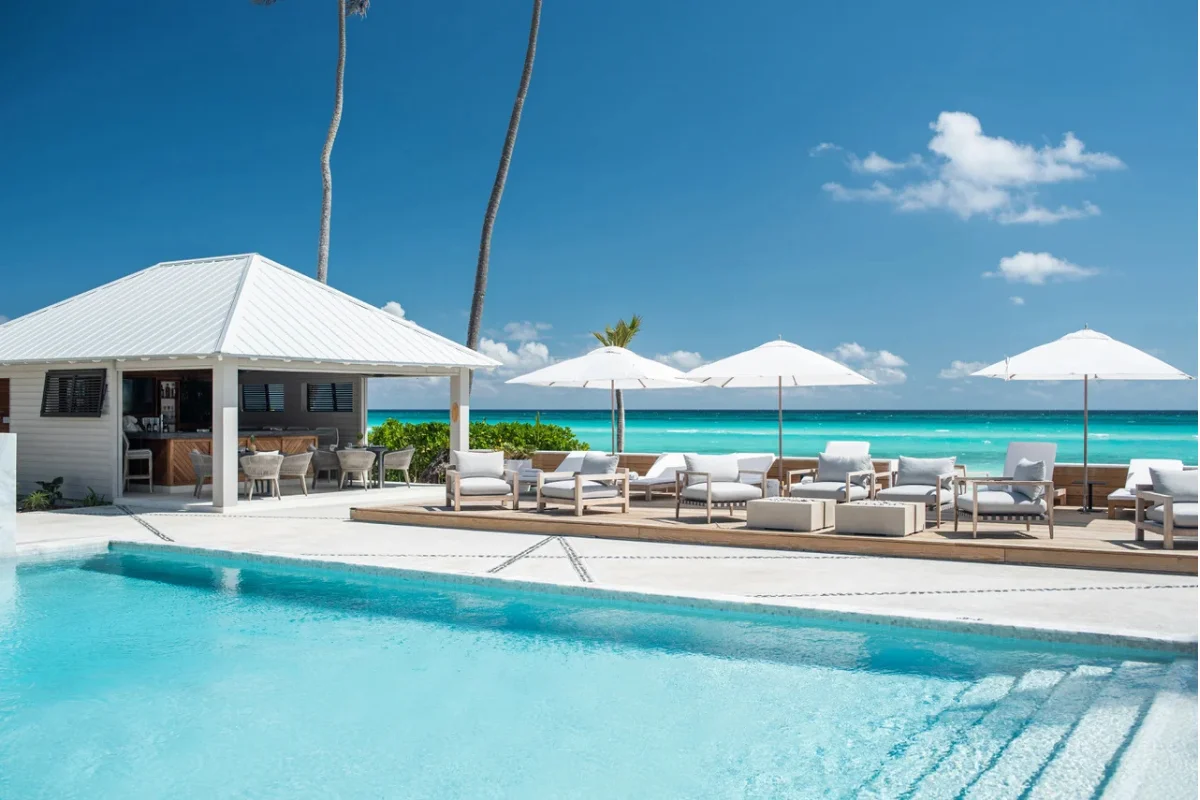 Beachfront hotel pool deck with outdoor lounge chairs, umbrellas, and comfortable seating overlooking turquoise water