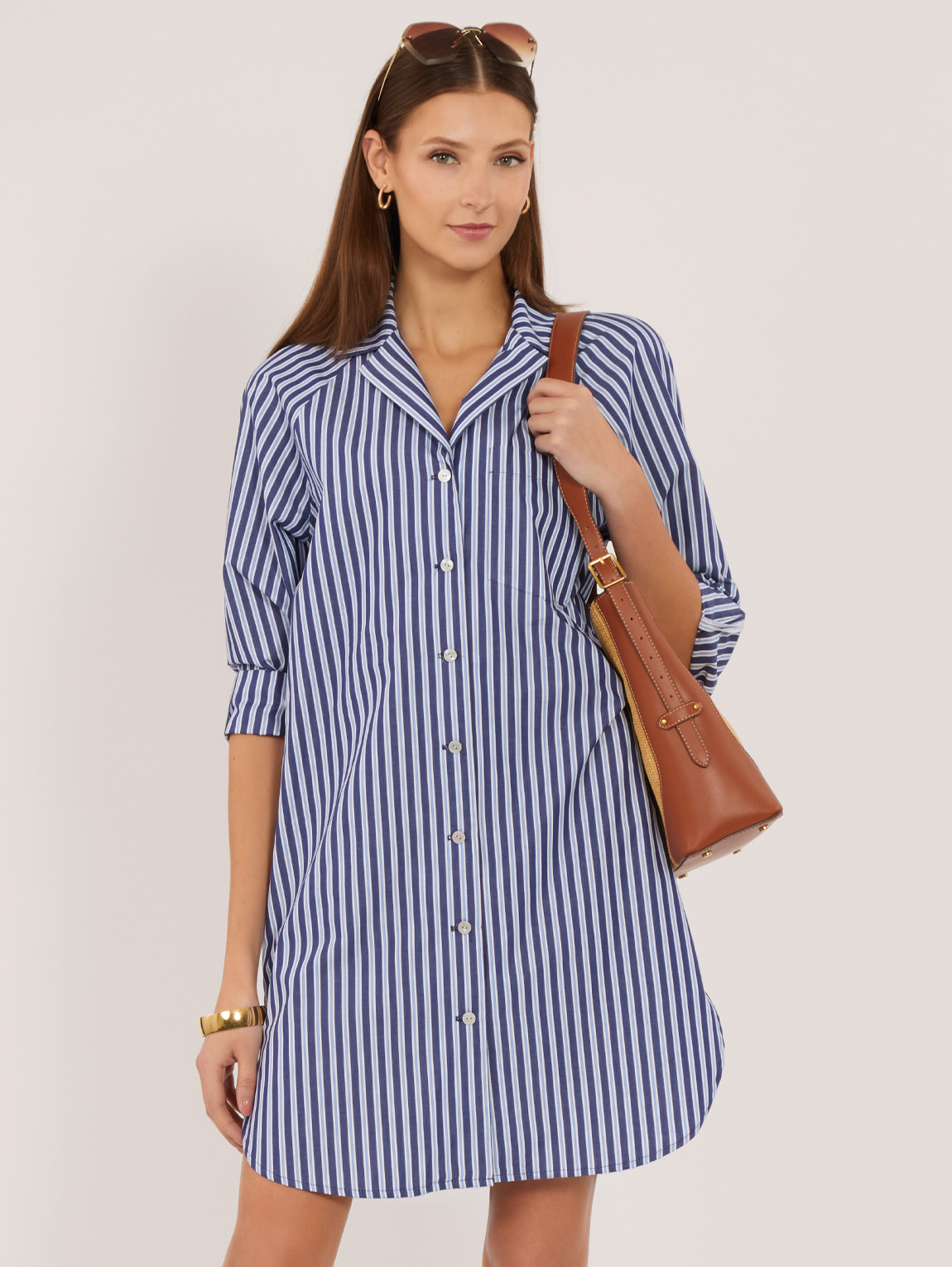 Woman in a striped shirt dress holding a brown handbag.