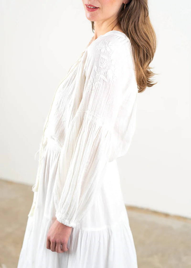 A model wearing a white floaty bohemian long sleeved blouse with balloon sleeves, fitted cuffs and embroidery details.