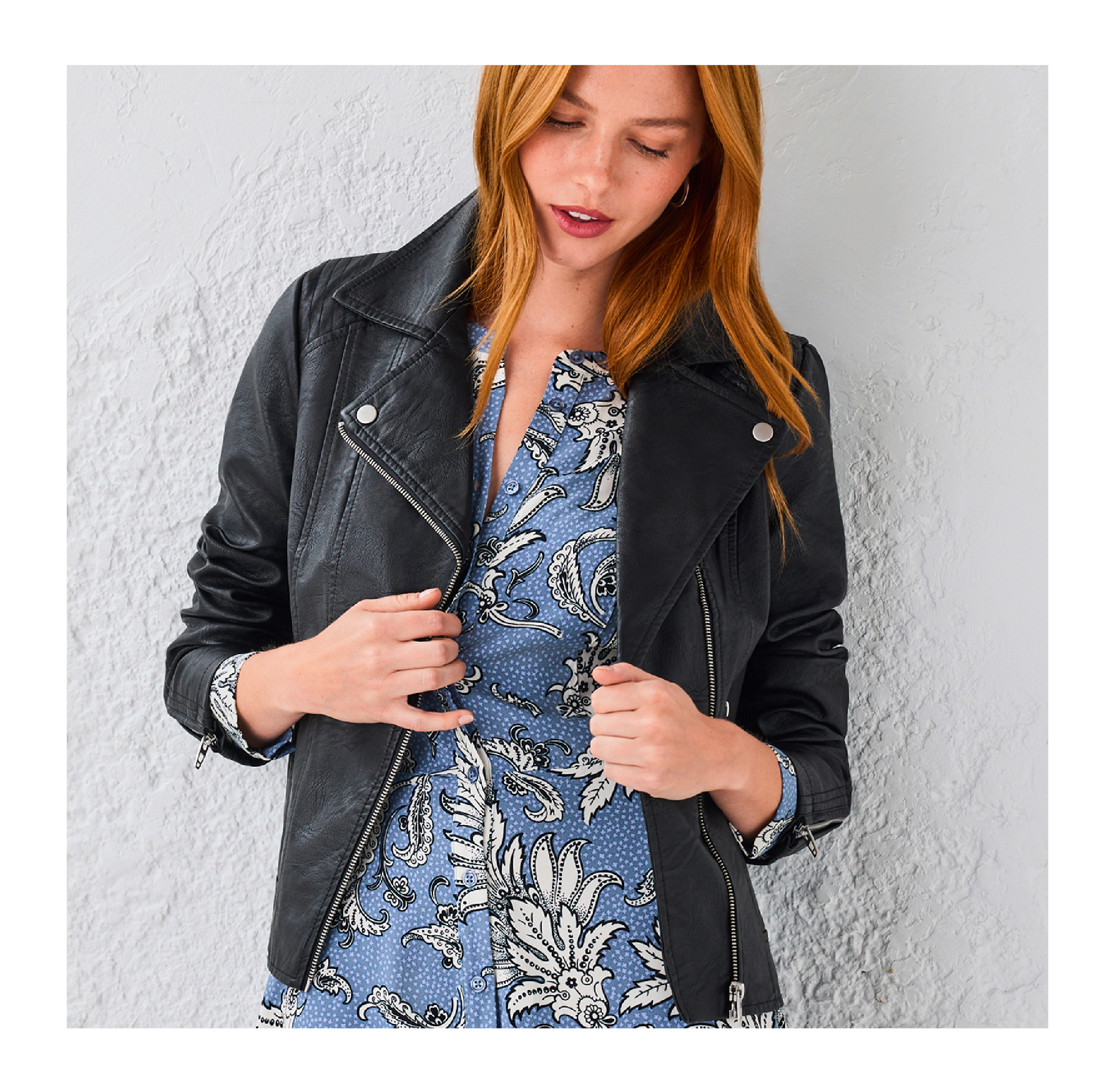 A woman in a black leather jacket over a blue floral dress.