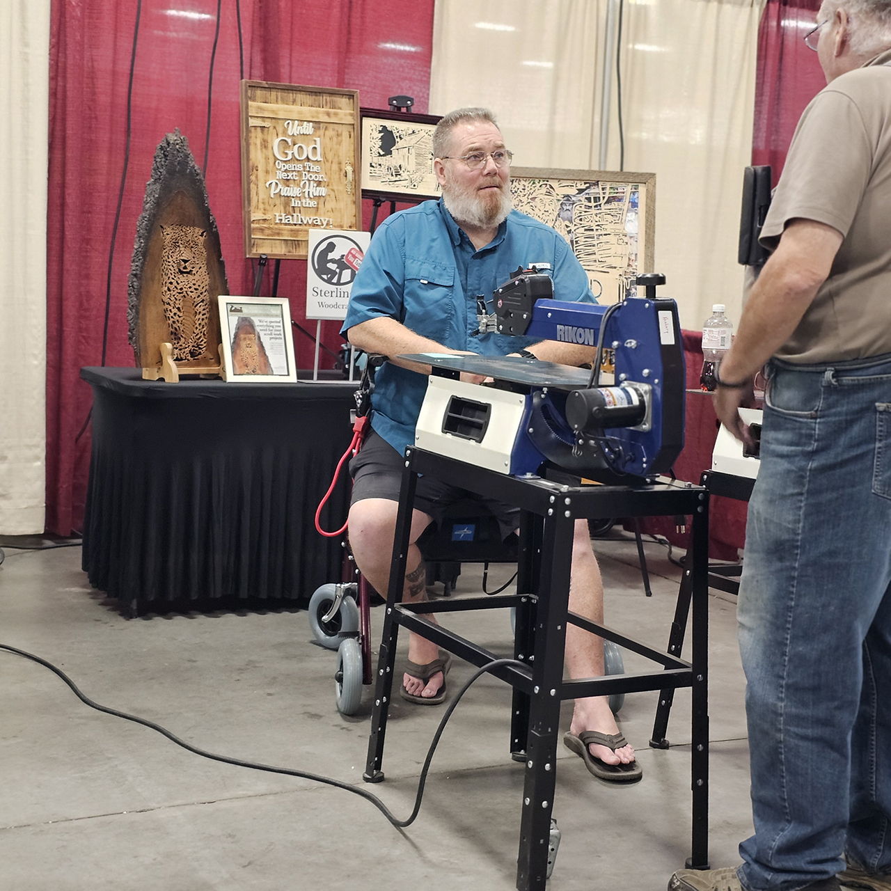 Man demonstrating a machine at an exhibition, seated and interacting with another person.