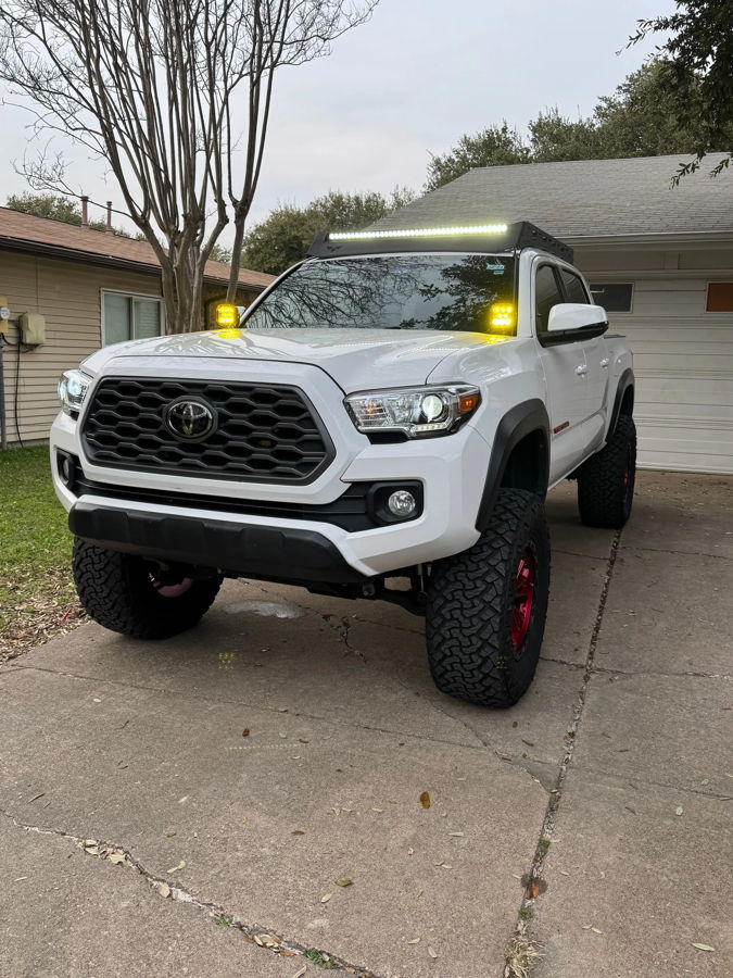 Front three-quarter white lifted Toyota Tacoma red wheels roof rack LED light bar ditch lights concrete driveway Joel's 2-Chime 3-Liter featured gallery photo 1