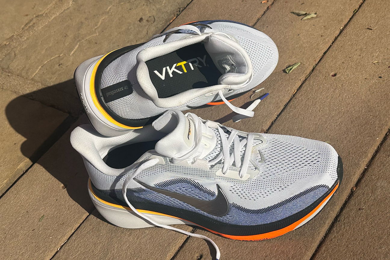 A pair of white and orange athletic shoes on a wooden surface.